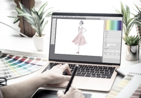 A person using a laptop and stylus to create digital art with plants in the background.