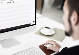 A person working on a computer in an office with a coffee cup nearby.