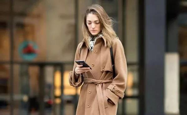 Woman in camel trench coat using phone in city