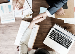 Business handshake over desk with laptop and documents