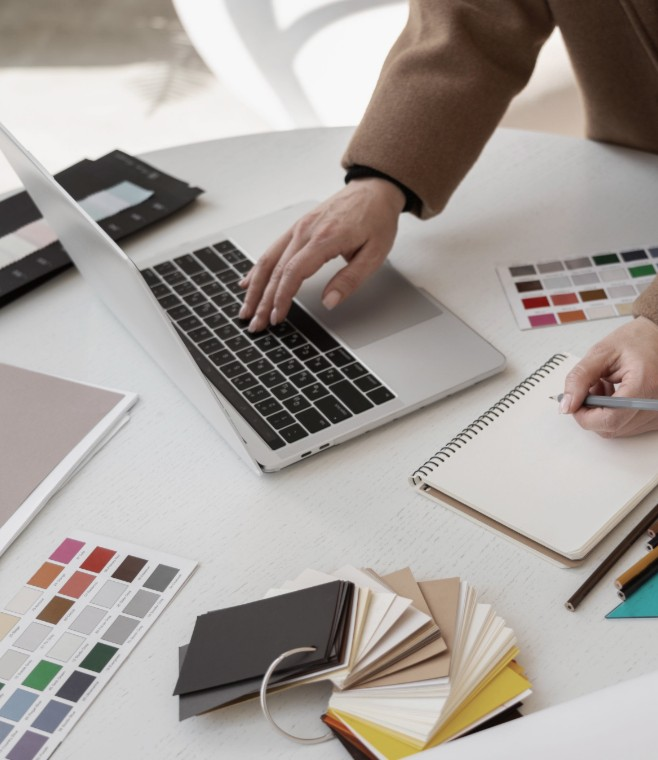 Hands working on a laptop with color swatches and notebooks, showing a design process.
