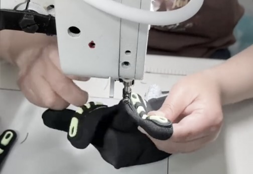 Hands sewing black gloves on a machine
