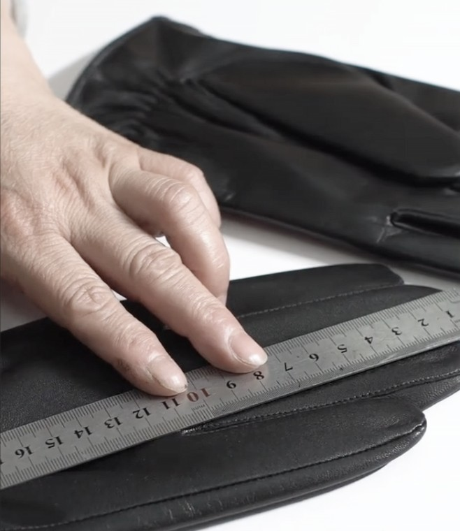 Hand measuring a black leather glove with a ruler for quality control.