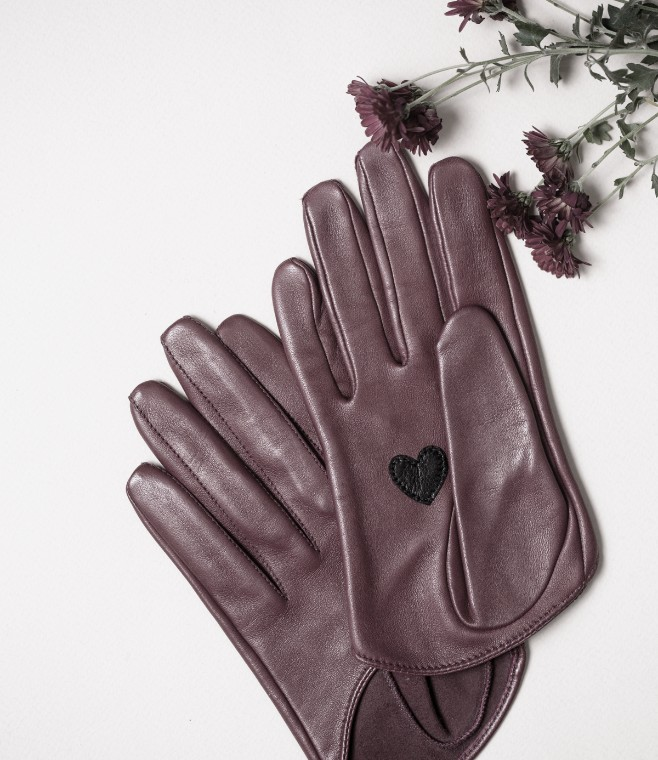 Purple leather gloves with a black heart appliqué, beside a small branch of purple flowers.