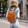 Model wearing tan leather backpack on city street