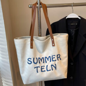 Canvas tote on garment rack, off-white body with embroidery and long shoulder straps.