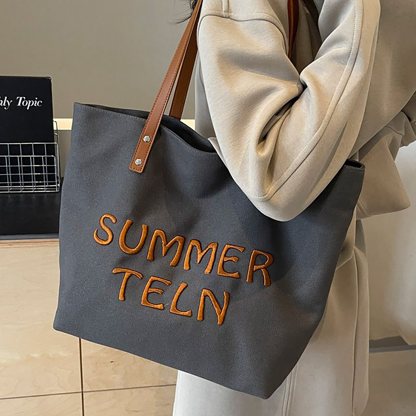 Model carrying grey canvas tote with embroidered text, shoulder-carry work tote.