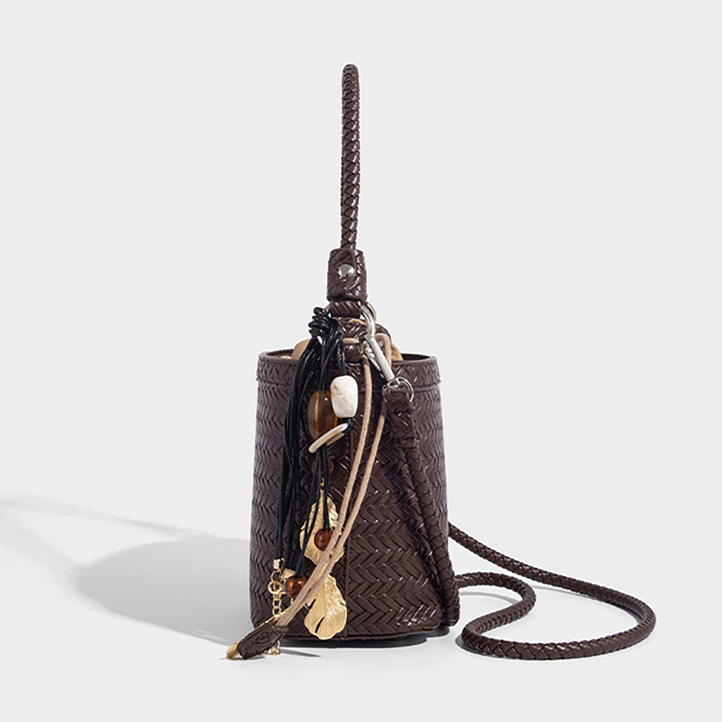 Side view of woven bucket bag with tassel charm and ring hardware for strap.