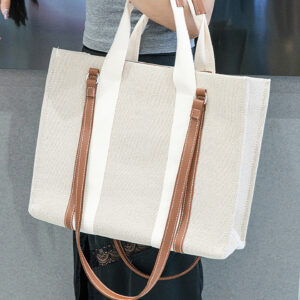 Model carrying large beige canvas tote bag with brown trim, showing versatile shoulder strap