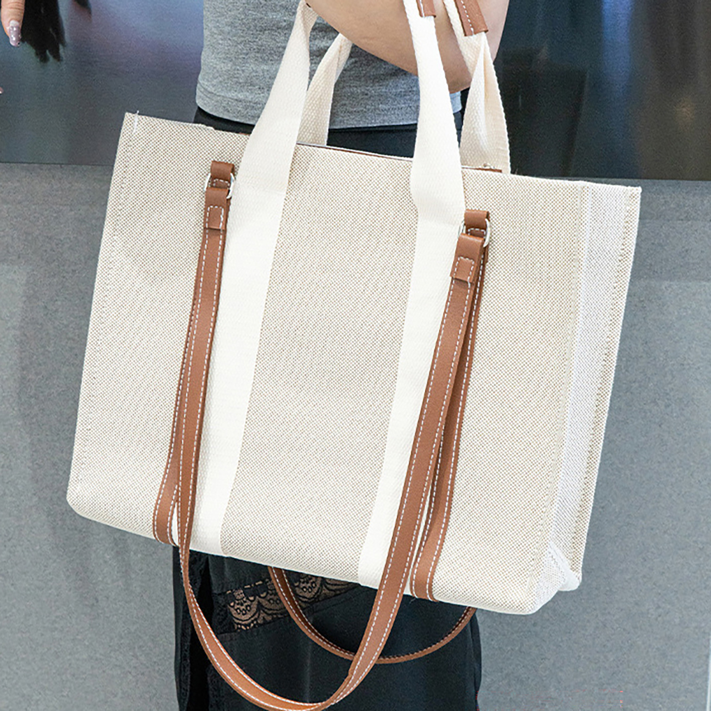 Model carrying large beige canvas tote bag with brown trim, showing versatile shoulder strap