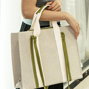 Side view of model with large beige canvas tote bag featuring green leather trim and comfortable handles