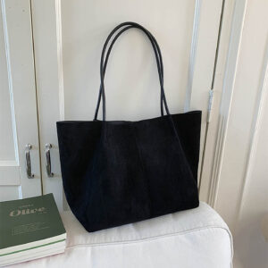 Black suede tote bag displayed on table with books for women's daily use