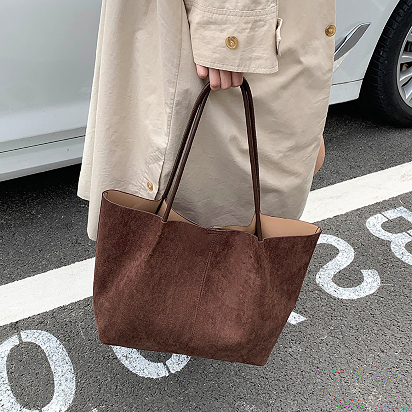 Woman carrying brown suede tote bag by hand in outdoor parking area