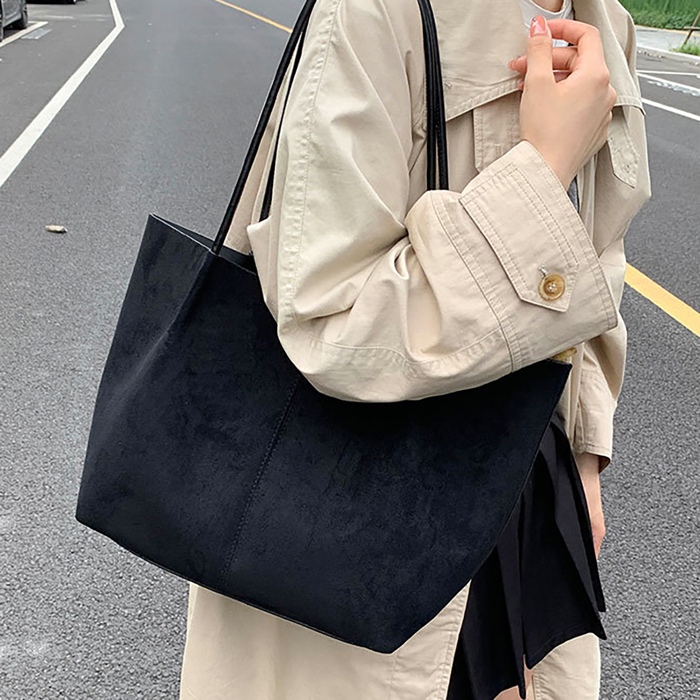 Woman wearing black suede tote bag on shoulder outdoors for commuting