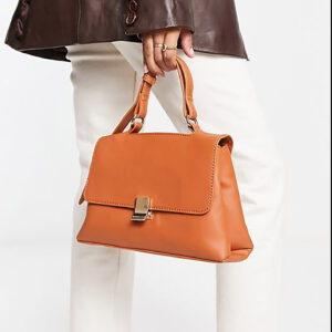 Model holding tan vegan leather top-handle bag with magnetic-snap flap.