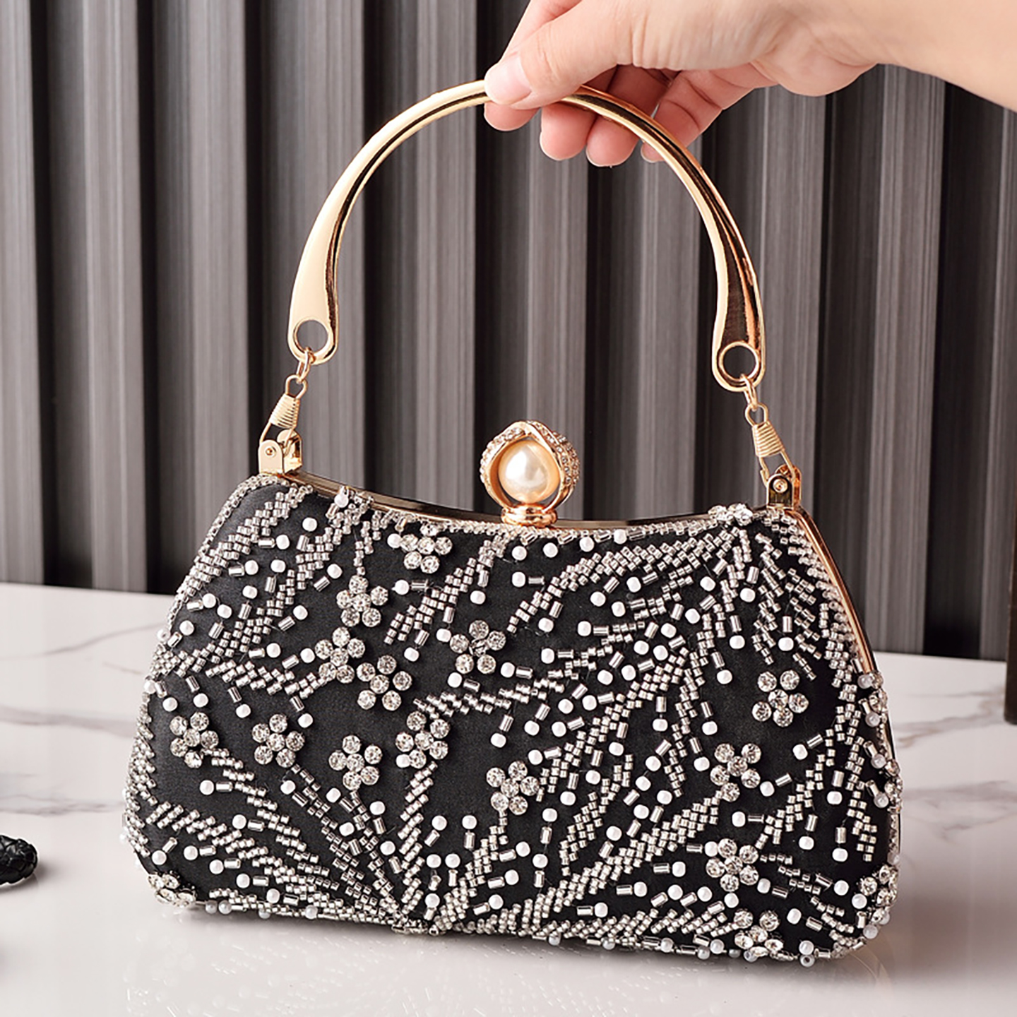 Top-handle black beaded clutch bag with pearl clasp held in hand.