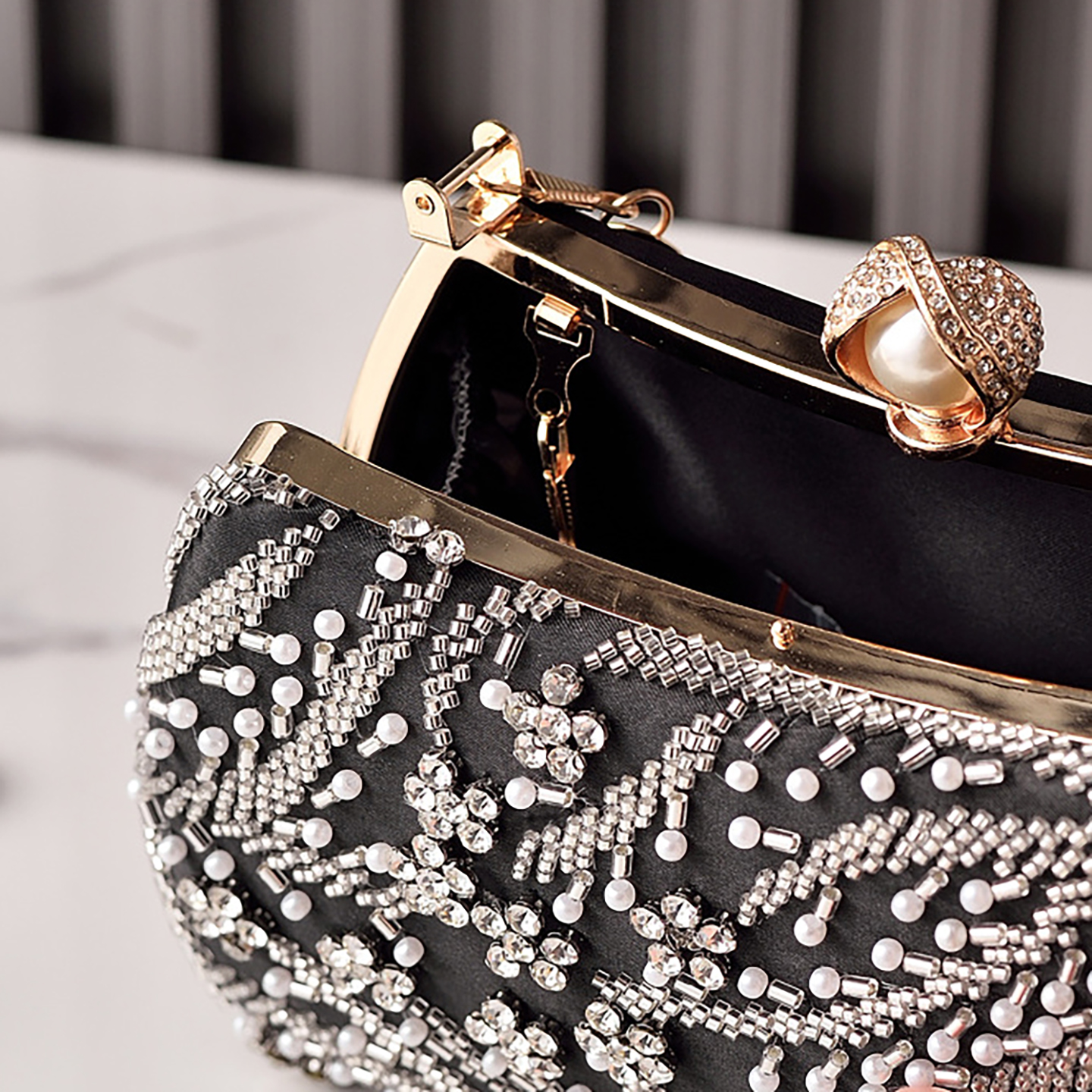 Close-up of pearl kiss-lock and metal frame on black beaded clutch.
