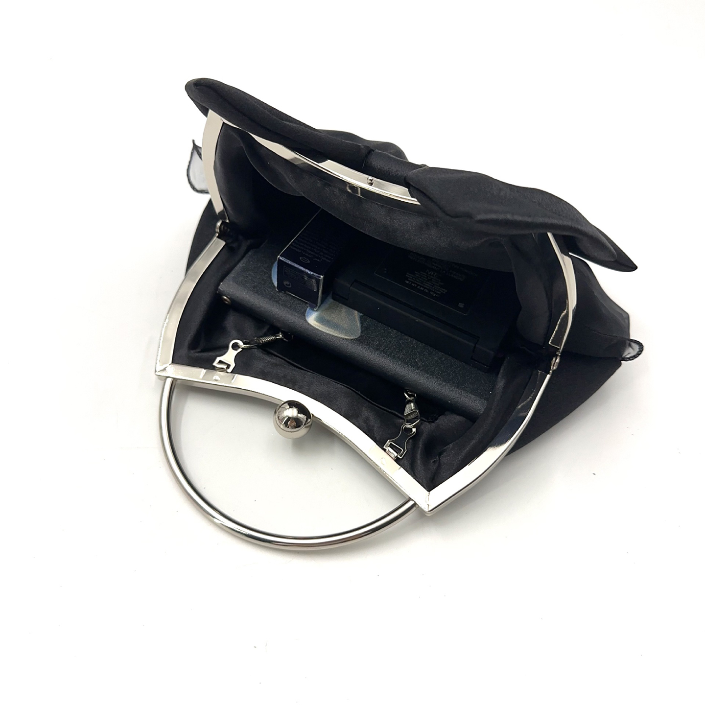Open view of black satin evening clutch showing interior pocket with phone and lipstick for practical use