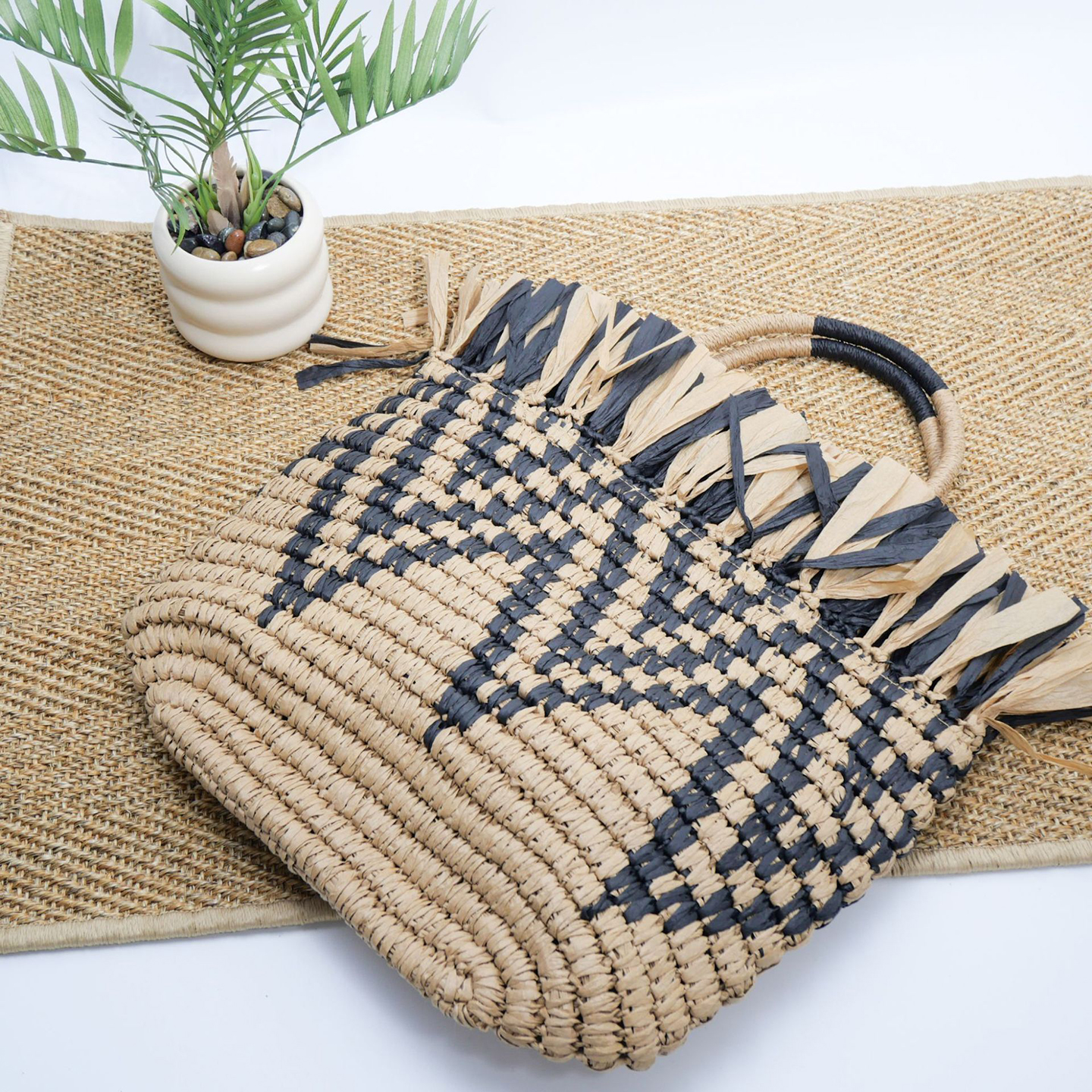 Angled view highlighting woven pattern and raffia fringe detail of the tote.